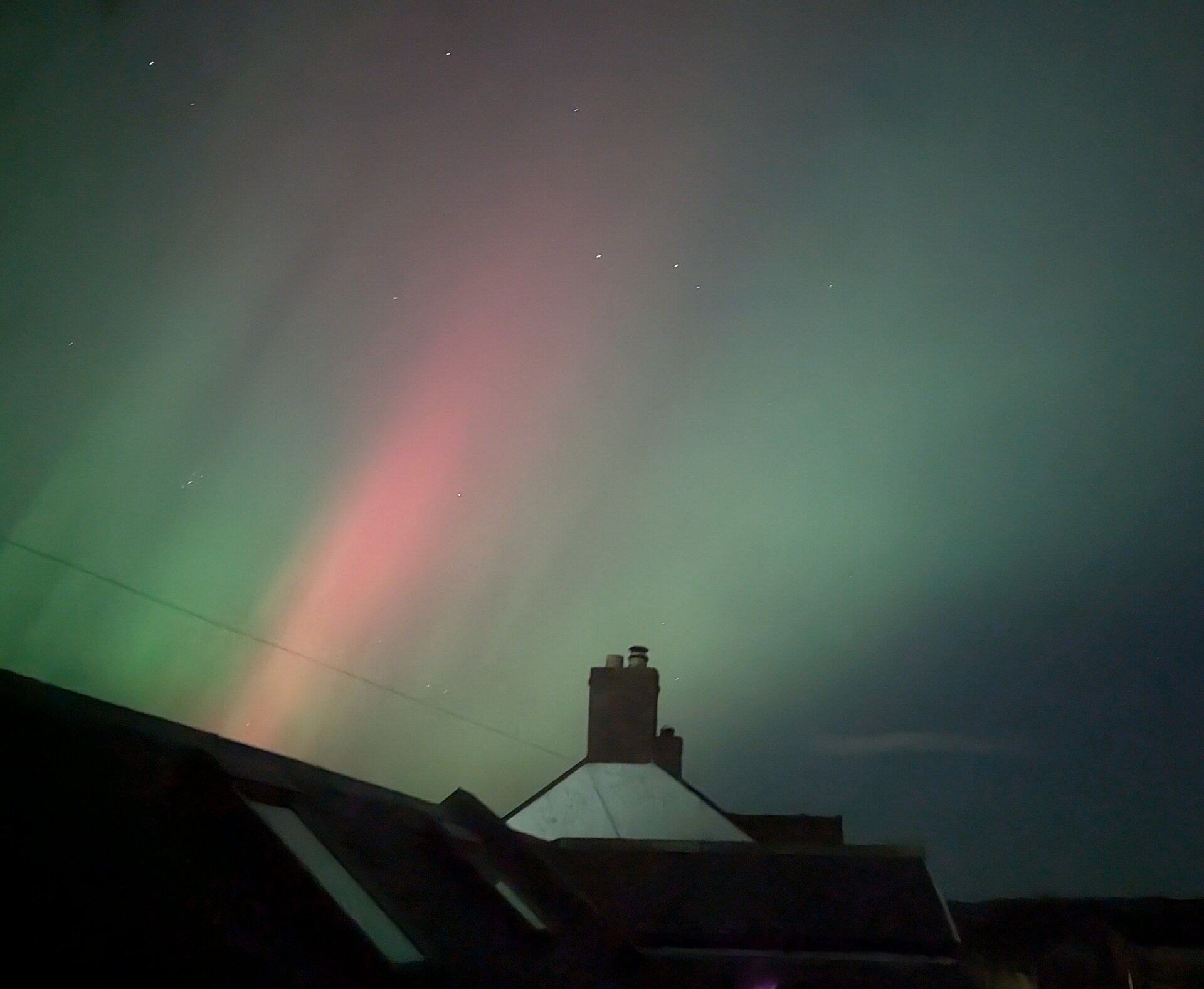 Green and pink northern lights over a rooftop and chimney in Wark, Northumberland